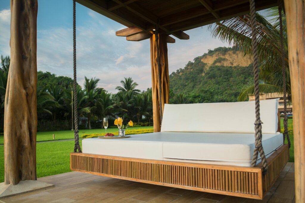 A luxurious swing bed under a wooden canopy with tropical palm trees.